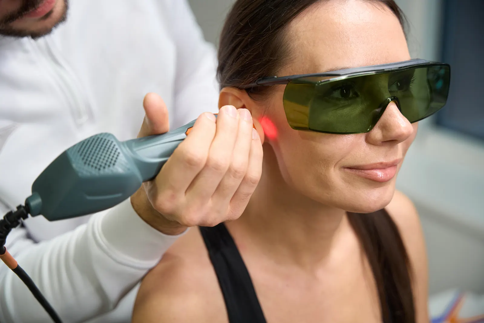 Low-level laser therapy handpiece with a visible red glow, eye protection on